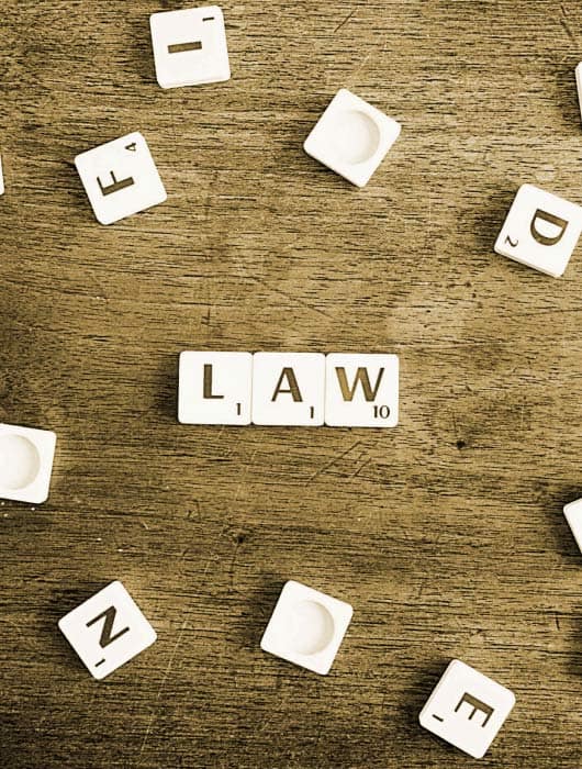 Gioco di lettere con la parola 'LAW' evidenziata tra le tessere bianche su un tavolo di legno, rappresentando concetti legali.