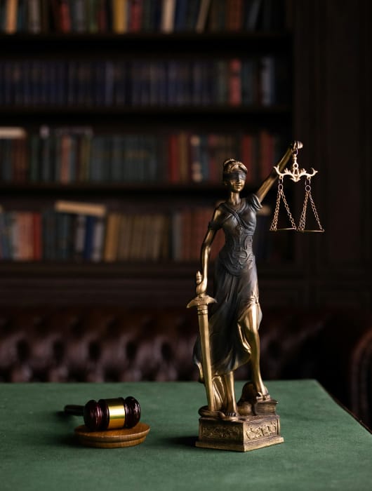 Statua della Giustizia che tiene una bilancia e una spada, simbolo di equità e legge, con un gavel in primo piano.